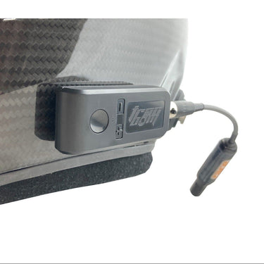 A Trac-Com Chaser Bluetooth lead/follow package device attached to the side of a racing suit, showing the small rectangular Bluetooth box with a cable and button interface.